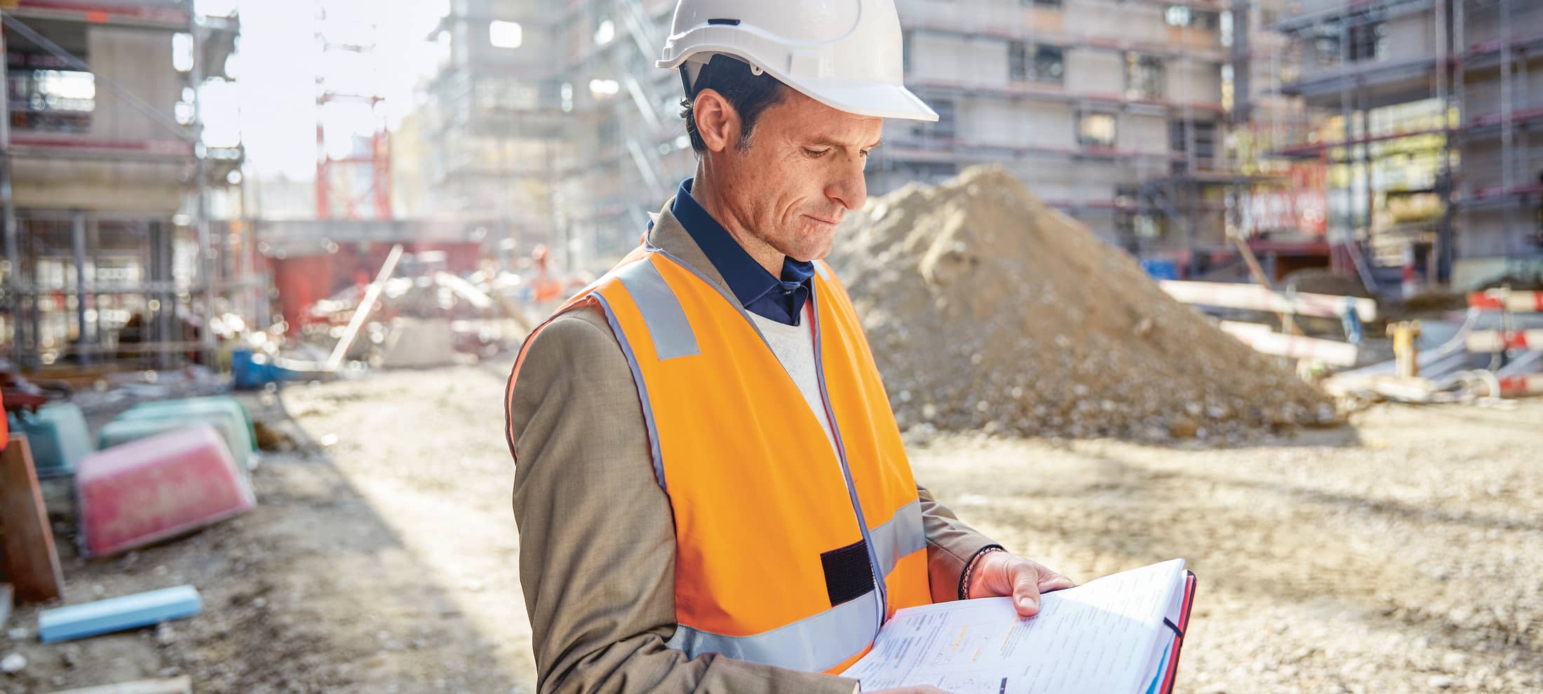 Uomo con il casco di sicurezza e il giubbotto controlla documenti in un cantiere 