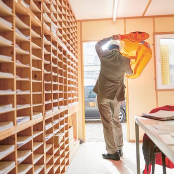 Rechtsschutz für Unternehmen: Architekt verlässt Bürocontainer auf Baustelle und zieht sich Leuchtweste und Helm an 