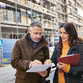 Rechtsschutz für Unternehmen: zwei Immobilienmakler besprechen sich vor einer Immobilie im Rohbau