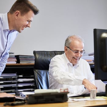 Rechtsschutz für Unternehmen: Gespräch zwischen zwei Mitarbeitern an einem Arbeitsplatz mit Computer