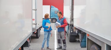 Rechtsschutz für Unternehmen: Mitarbeitende eines Transportunternehmens besprechen sich zwischen parkierten Lastwagen