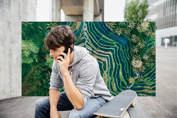 Giovane uomo seduto a terra con lo skateboard e telefona con il cellulare